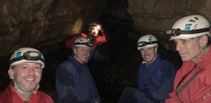 4 men in cave suits and helmets with torches, in a cave