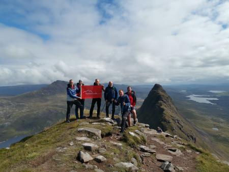 Small group with OutdoorLads flag at the summit of An Teallach