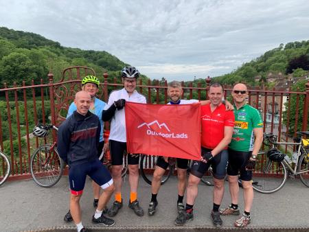 Group in lycra and helmets holding OutdoorLads flag