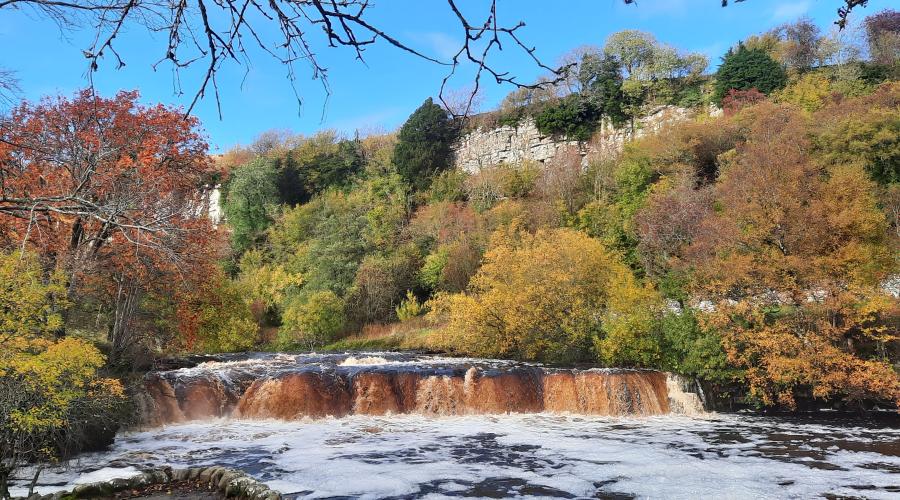 Autumn colours at wide waterfall , blue sky above