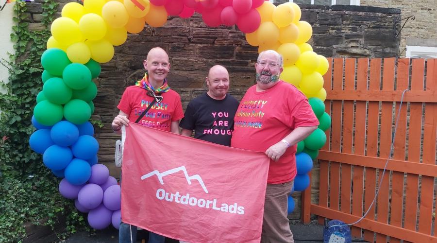 Three guys with Outdoorlads flag in front of a circular pride balloon display