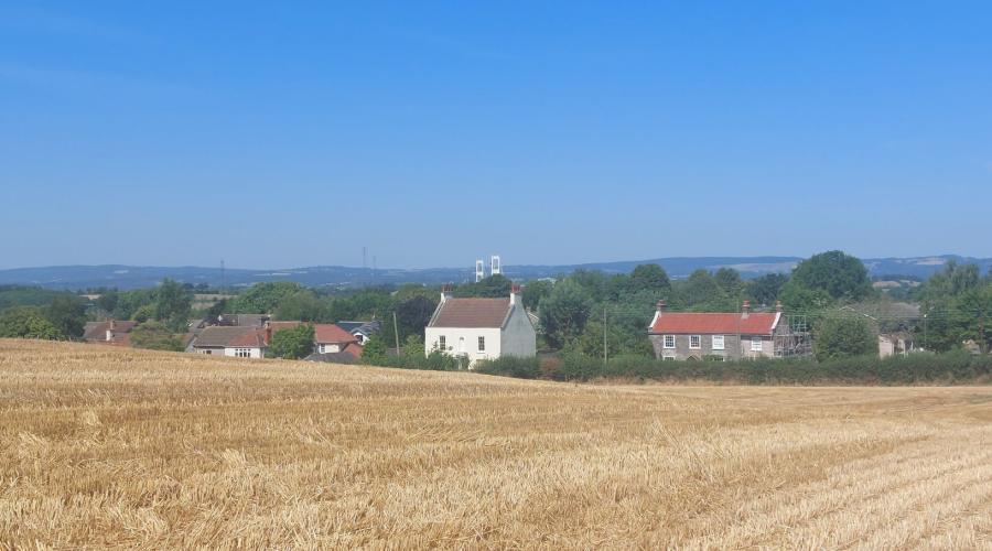 A ploughed field, some houses and Severn Bridge in distance
