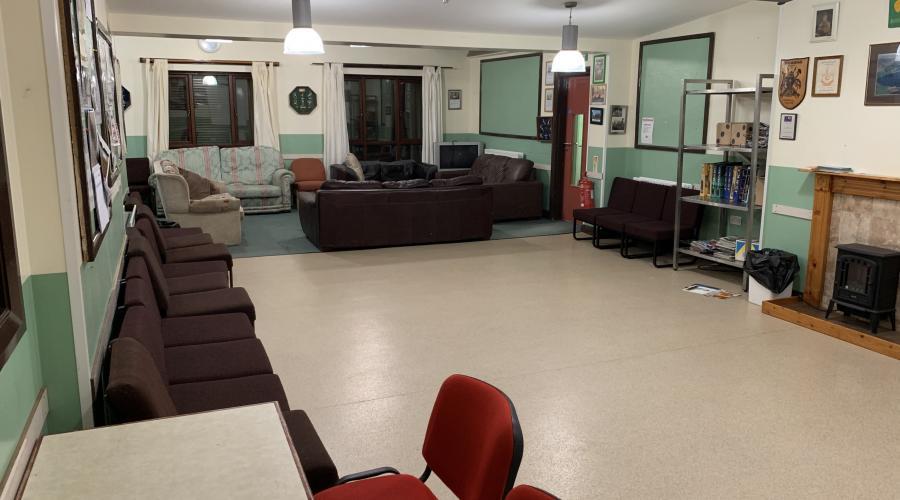 A room with white linoleum flooring and chairs lining one wall, with sofas in a seating area at the far end of the room.