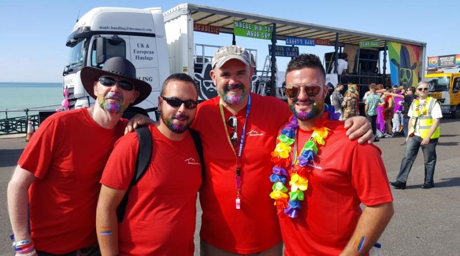 4 men in red t shirts smiling with pride float behind