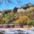 Autumn colours at wide waterfall , blue sky above