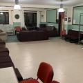 A room with white linoleum flooring and chairs lining one wall, with sofas in a seating area at the far end of the room.