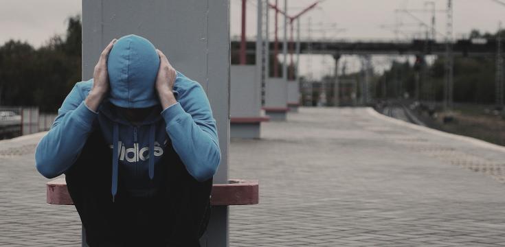 person at railway station in hoodie with head down